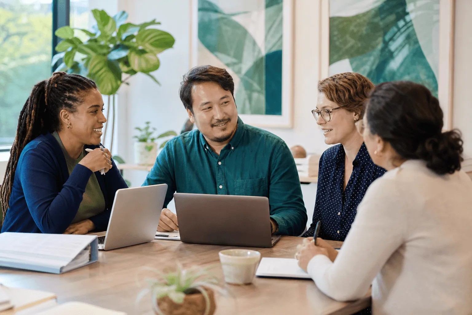 A small multidisciplinary clinical team collaborating around a table with laptops and notes in a bright modern office.