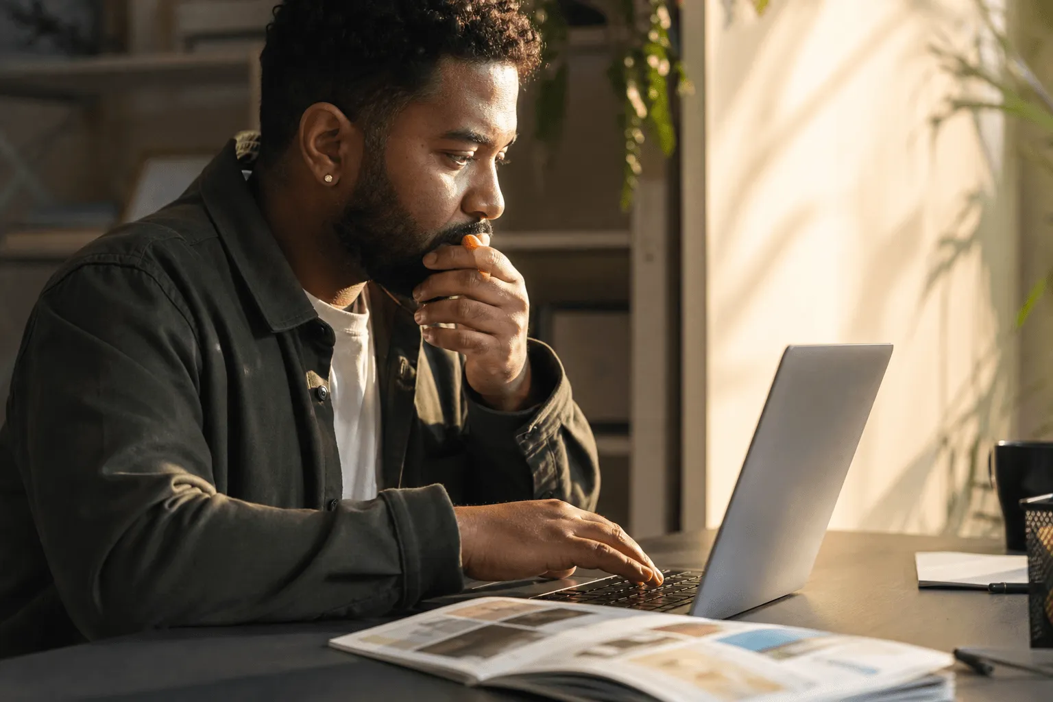 An adult thoughtfully drafting a message on a laptop with a printed service leaflet beside them.