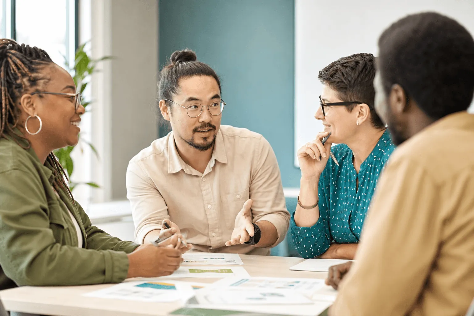 A small diverse group in discussion around a table with handouts at a professional training workshop.